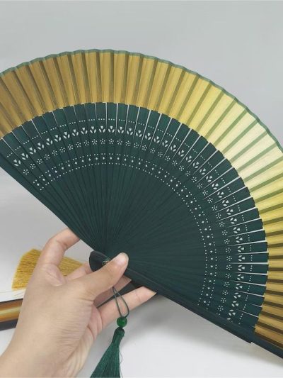 A folding fan with cutouts in dark green and gold.